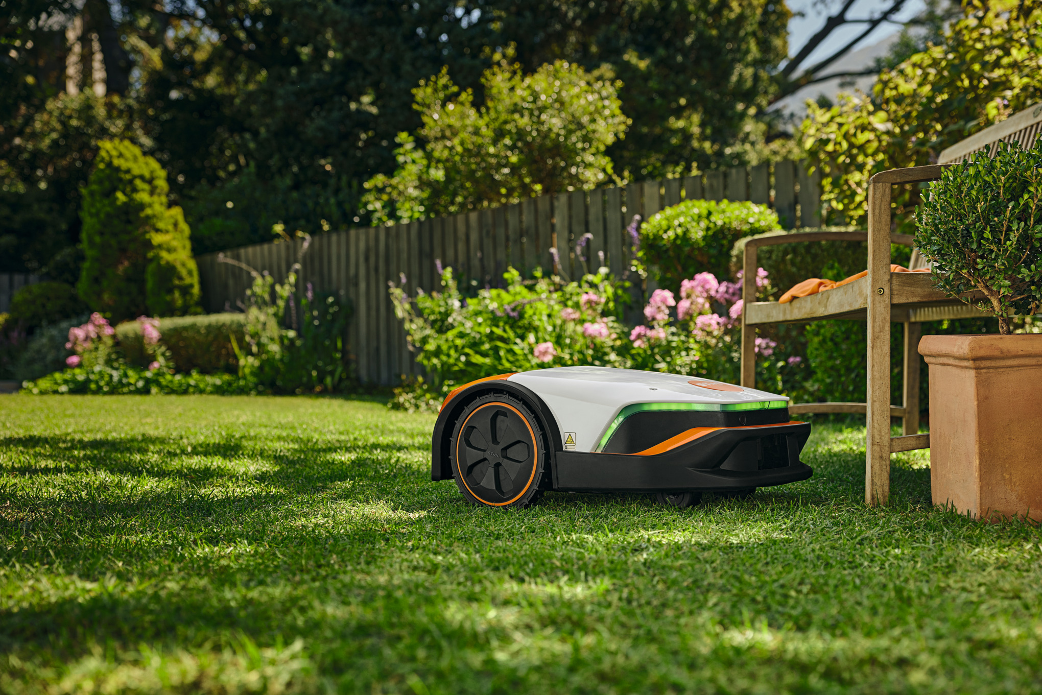 STIHL iMOW 7 Mähroboter im Einsatz auf einem grünen Rasen in einem blühenden Garten