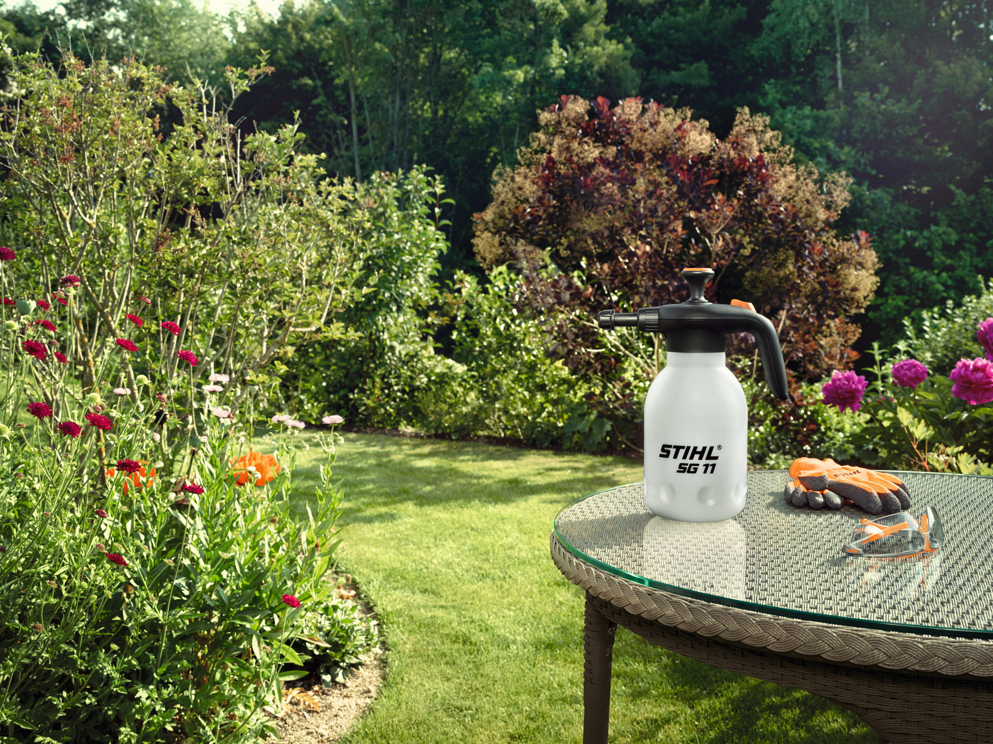 STIHL SG 11 Handspritzgerät auf Gartentisch umgeben von blühendem Garten