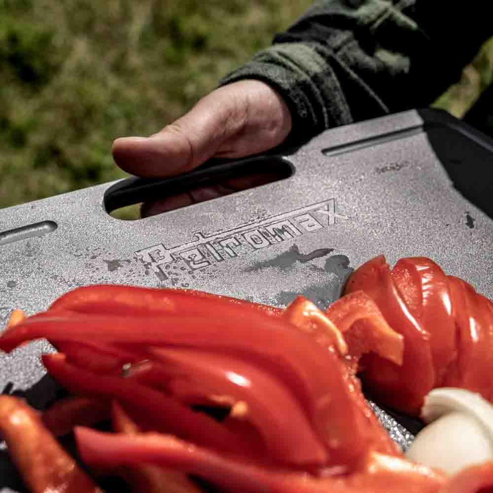 Hand hält Petromax Schneidebrett mit geschnittenen Paprika und Zwiebeln in der Natur