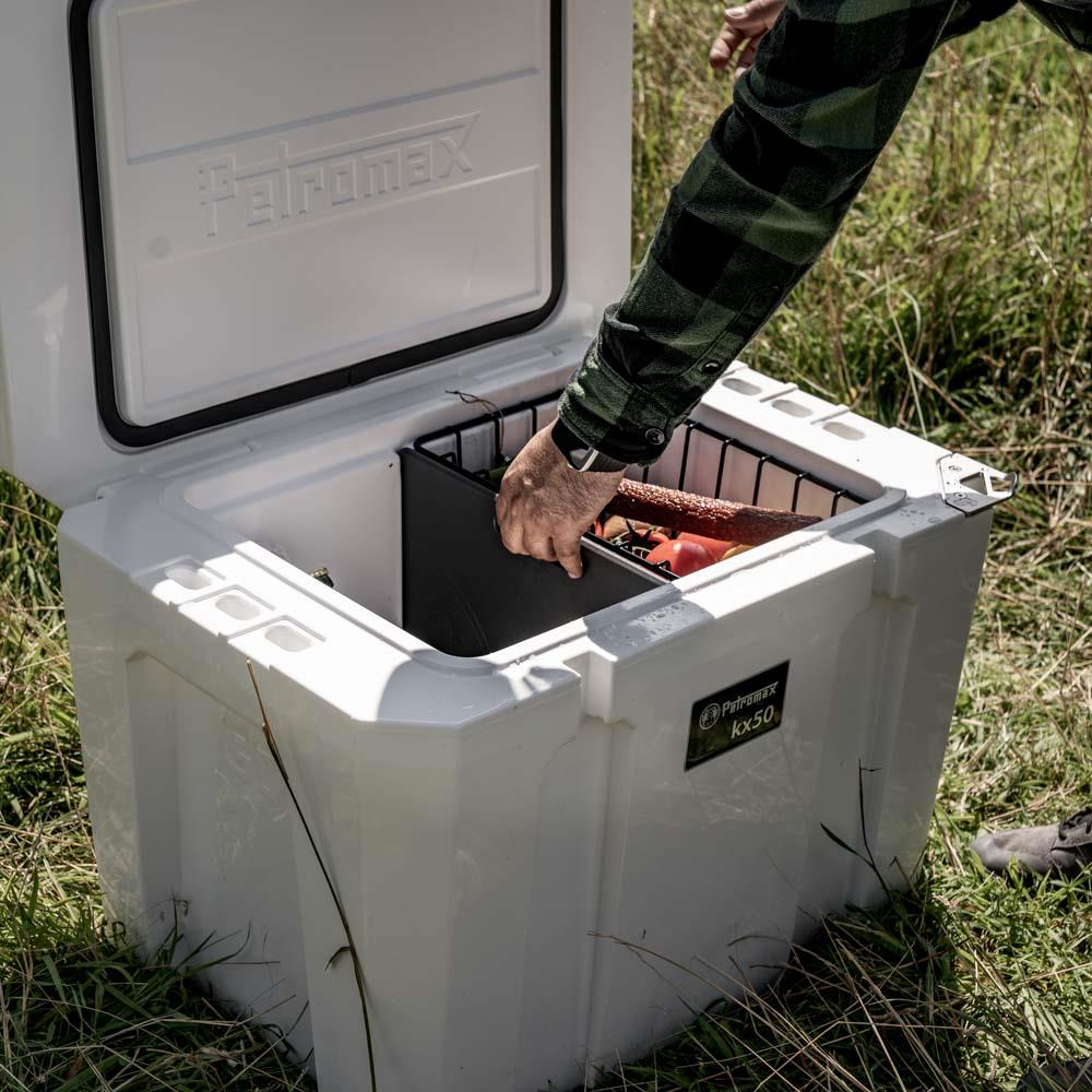 Person setzt Schneidebrett in Petromax Kühlbox ein, draußen mit Lebensmitteln darauf