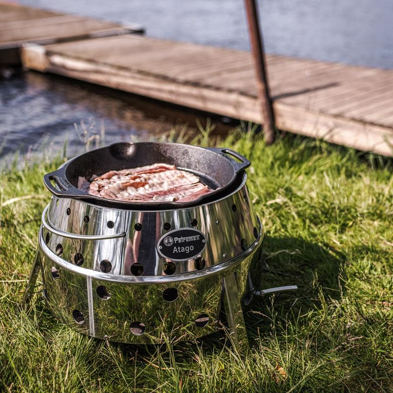 Petromax Grill-Feuerpfanne auf Atago Outdoor-Grill mit Speck am Seeufer