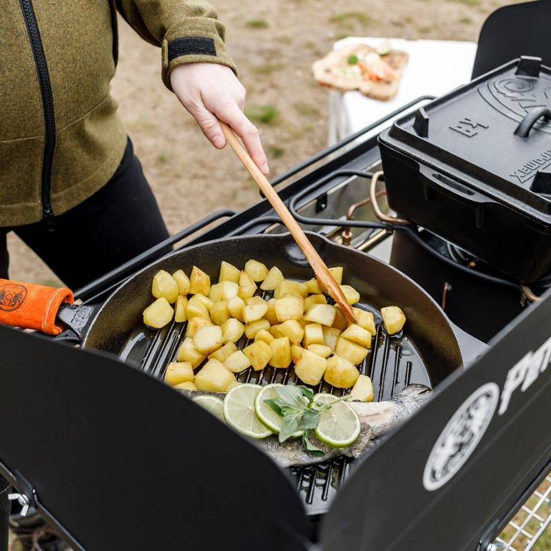 Person kocht Kartoffeln in Gusseisenpfanne auf Outdoor-Grill
