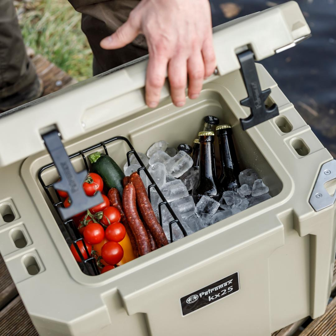 Hand öffnet Petromax Kühlbox kx25 mit Einsatzkorb voller Gemüse Würstchen Eis und Bier
