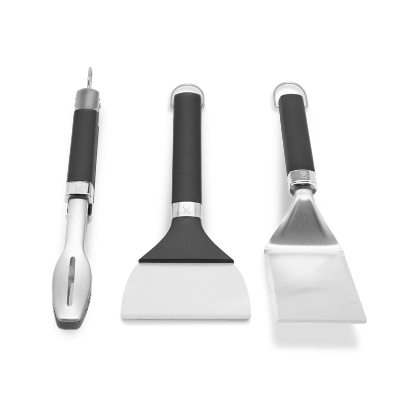 Weber Griddle Grillwerkzeug-Set mit Grillwender, Grillzange und Grillschaber auf grünem Hintergrund