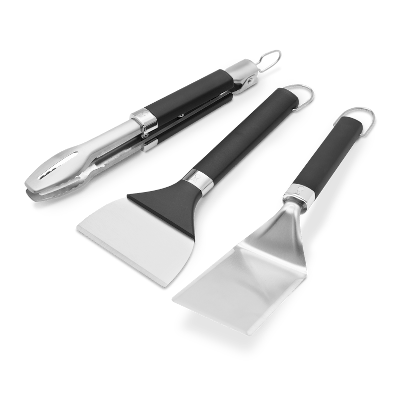 Weber Griddle Grillwerkzeug-Set mit Grillwender, Grillzange und Grillschaber auf grünem Hintergrund
