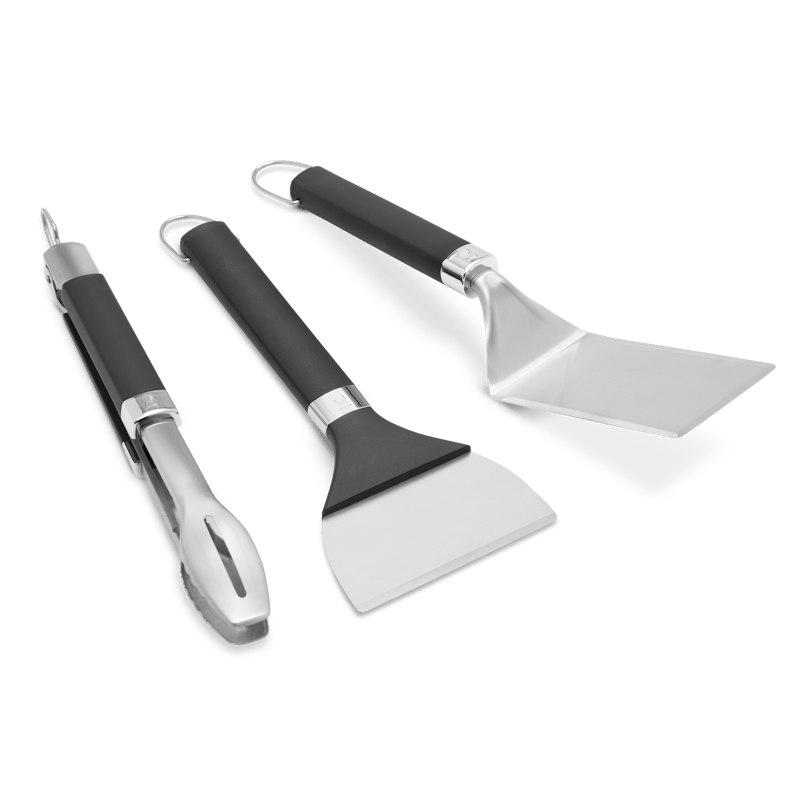 Weber Griddle Grillwerkzeug-Set mit Grillwender Grillzange und Grillschaber auf grünem Hintergrund