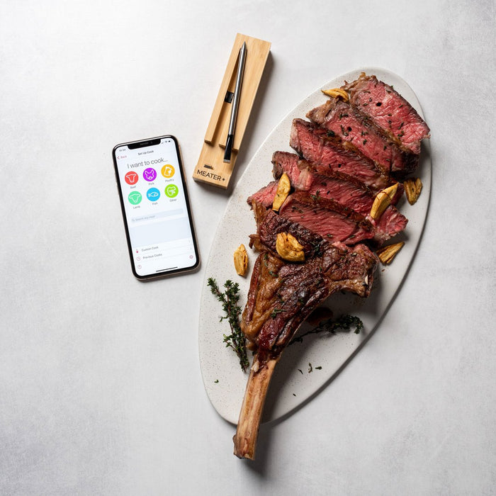 Smartphone mit App neben Tomahawk-Steak und MEATER Plus Thermometer