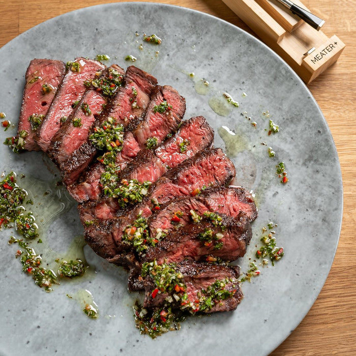 Aufgeschnittenes Rindersteak mit Chimichurri auf grauem Teller neben MEATER Plus Thermometer