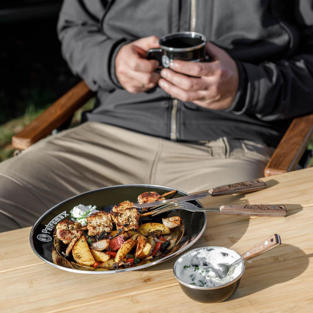 Mann beim Camping nutzt Petromax Besteck für Mahlzeit im Freien