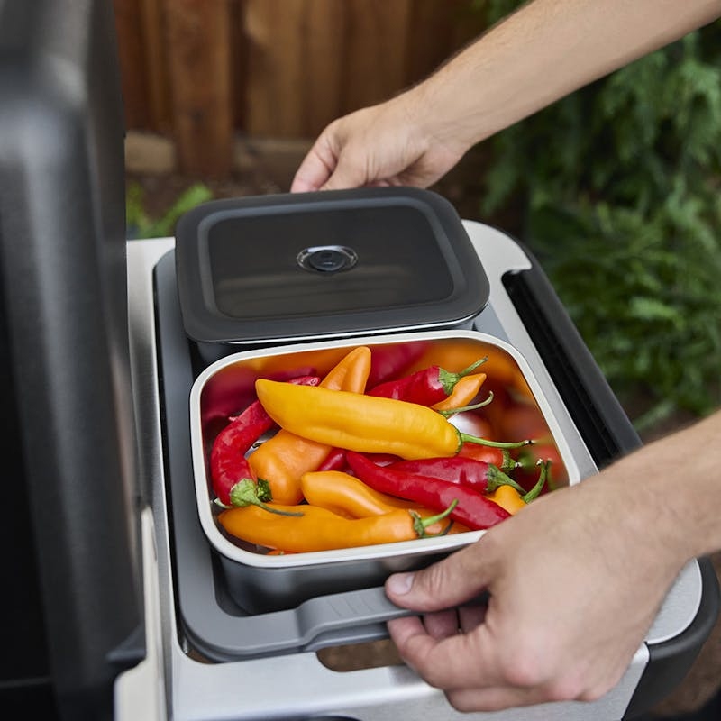 Hand setzt Deckel auf Edelstahlbehälter mit bunten Paprikas auf Weber Grilltisch