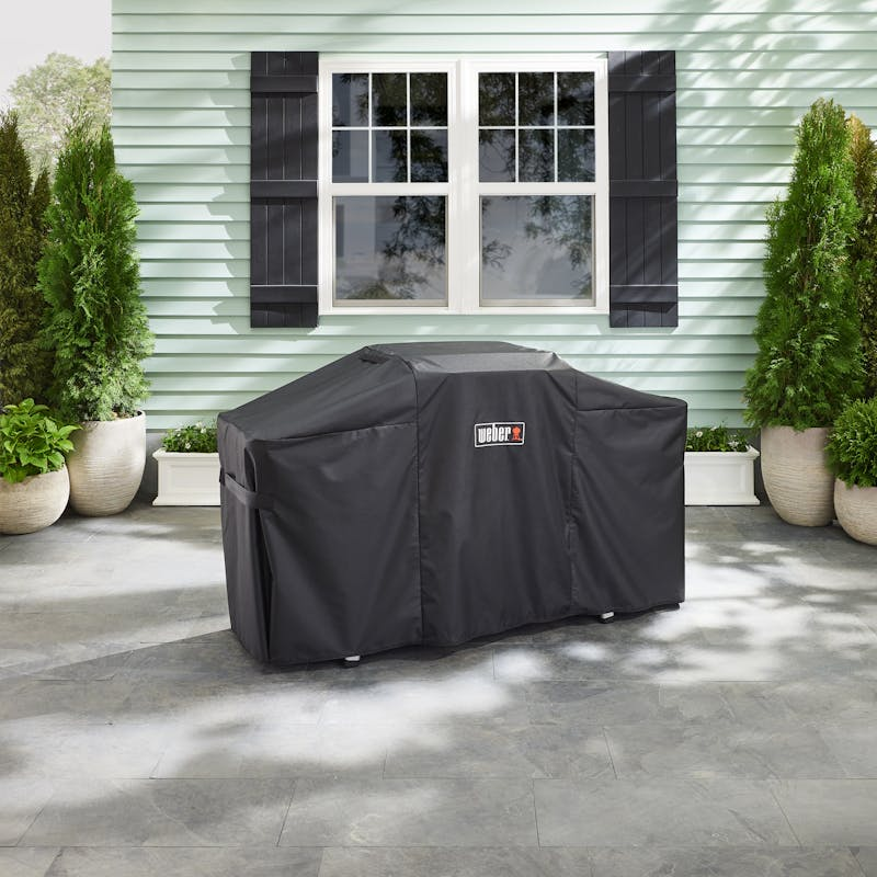 Weber Premium Abdeckhaube über Plancha auf Terrasse vor grünem Haus