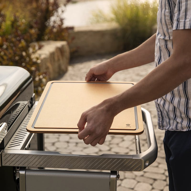Person legt Schneidebrett auf Grilltisch im Freien