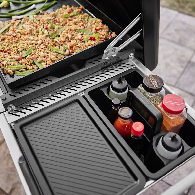 Weber Works Transportbehälter auf klappbarem Grilltisch neben Weber SLATE Plancha mit Gemüse-Reis-Pfanne
