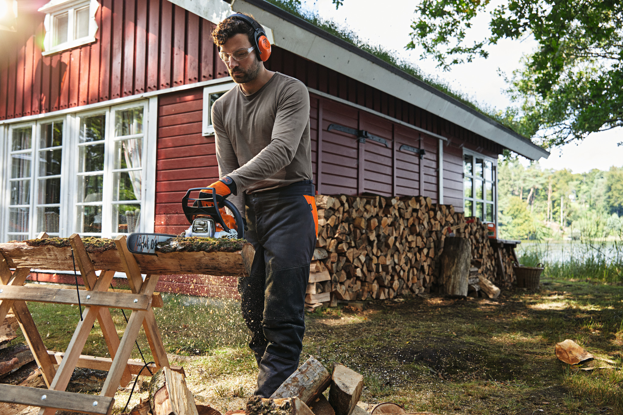 Mann benutzt Stihl Motorsäge zum Holzsägen vor rotem Holzhaus