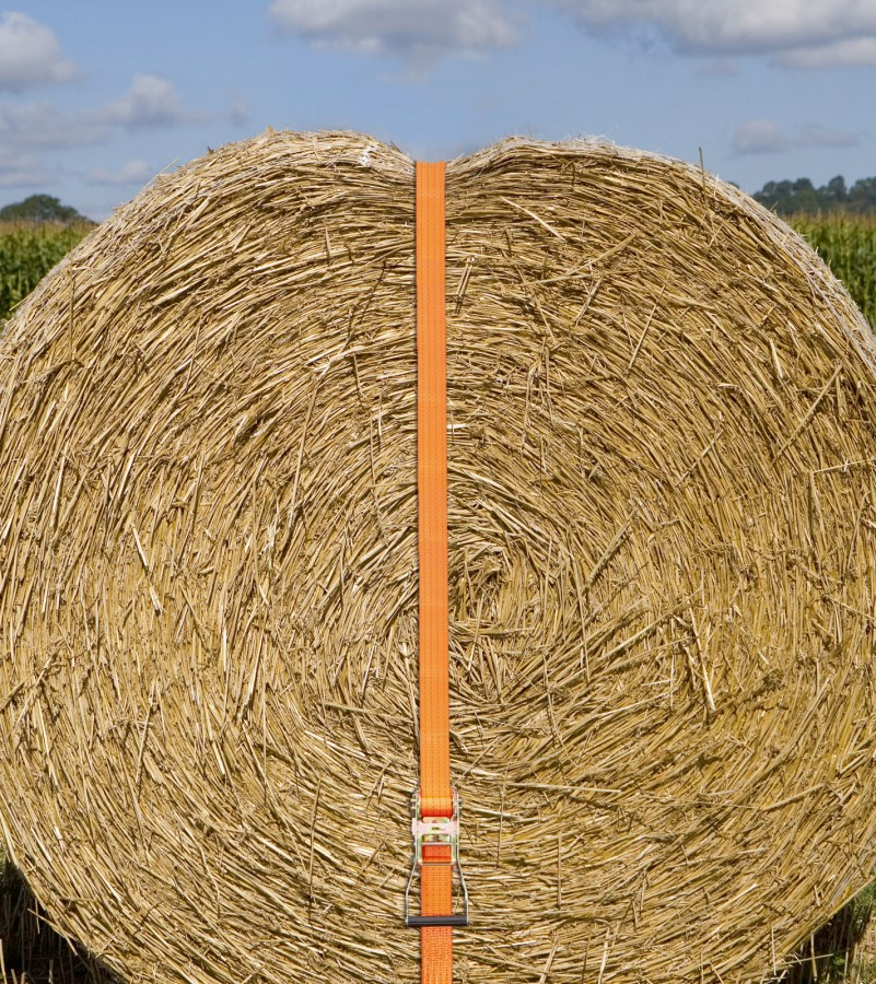 Orangefarbener Ratschenzurrgurt sichert großen Strohballen auf Feld