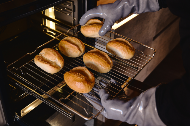 Person entnimmt Brötchen aus Ofen mit grauen Silikonhandschuhen