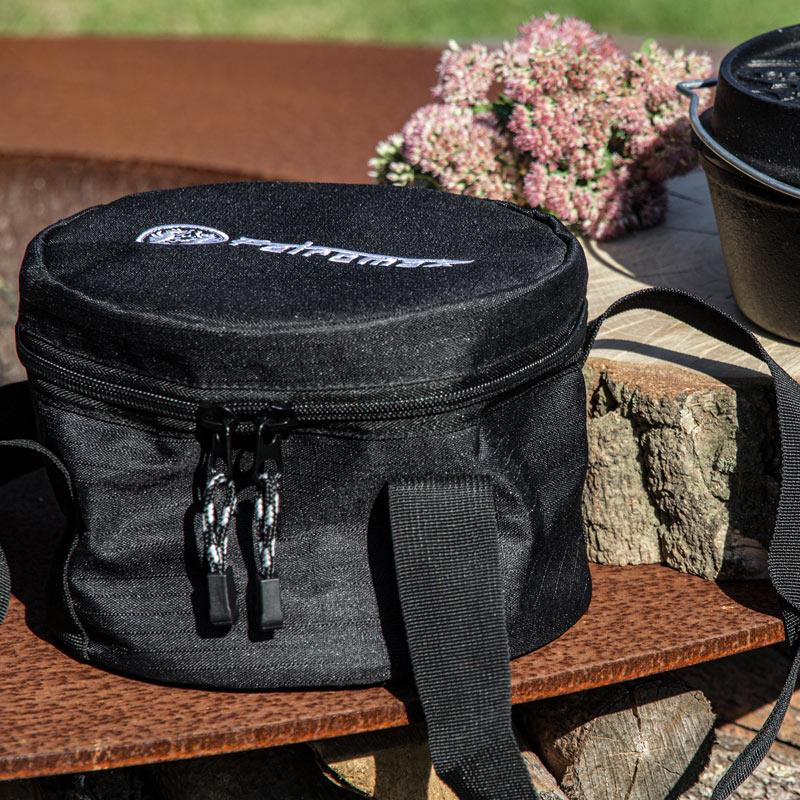 Schwarze Petromax Transporttasche für Dutch Oven auf Holzblock neben gusseisernem Topf