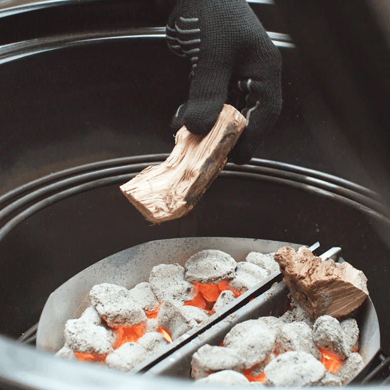 Person fügt Holz zu glühender Holzkohle in Weber Char-Baskets hinzu