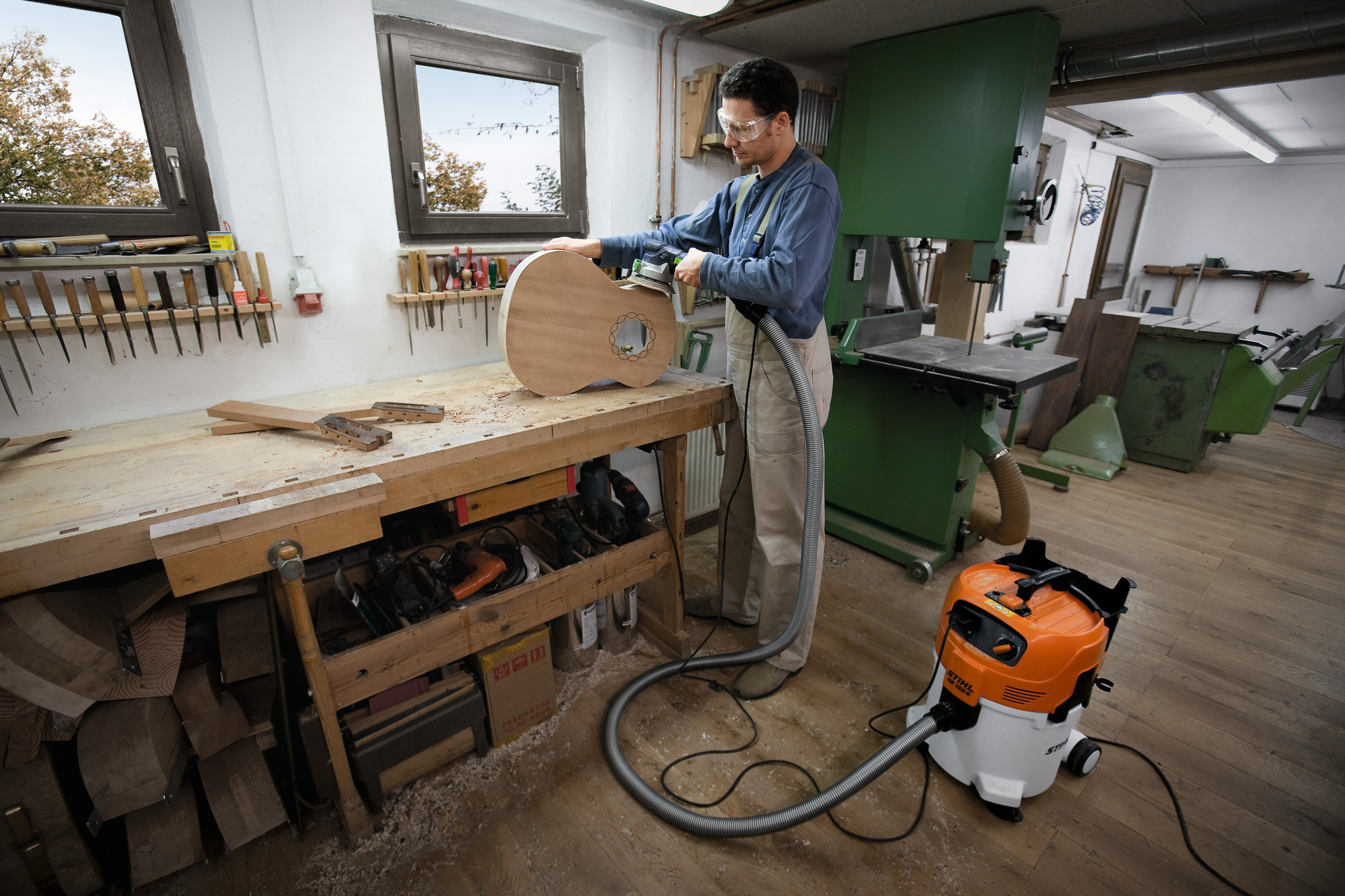Mann in Tischlerwerkstatt bearbeitet Holz neben STIHL SE 122 E Sauger