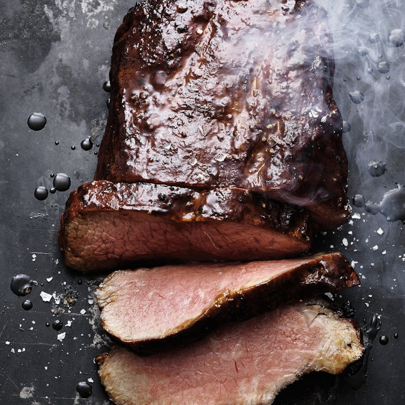 Gegrillter Rinderbraten in Scheiben auf dunklem Untergrund mit Rauch und Salz