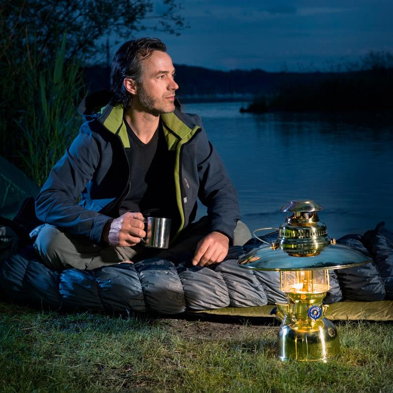 Mann sitzt am Seeufer bei Nacht neben Petromax HK500 Lampe