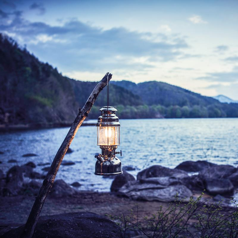 Petromax HK500 Petroleumlampe hängt an einem Ast am Seeufer bei Dämmerung