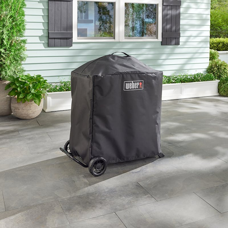 Weber Traveler Compact Gasgrill bedeckt mit schwarzer Weber Premium Abdeckhaube auf einer Terrasse