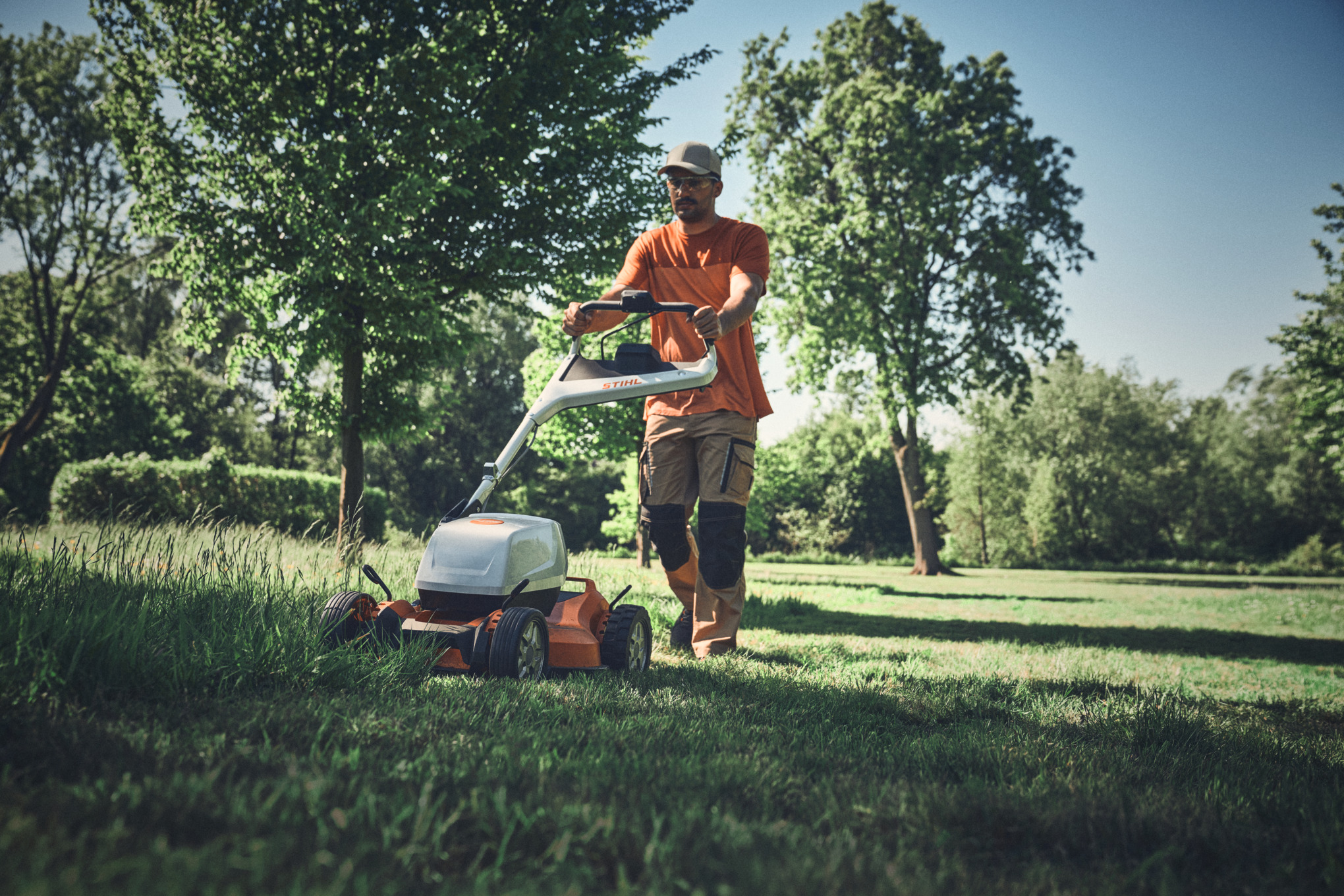 Mann benutzt STIHL Akku-Mulchrasenmäher in einem sonnigen Park