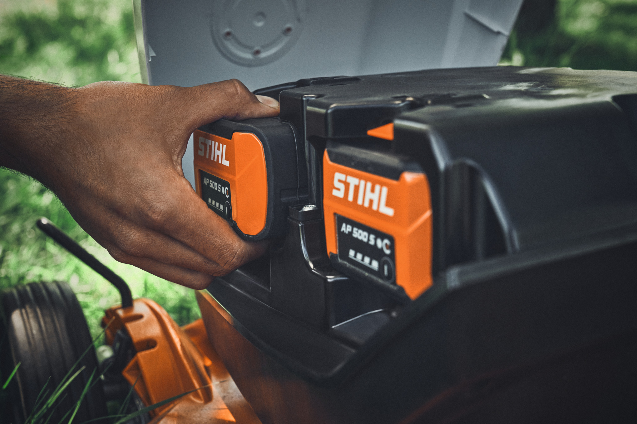 Person setzt STIHL Akkus in einen Rasenmäher ein