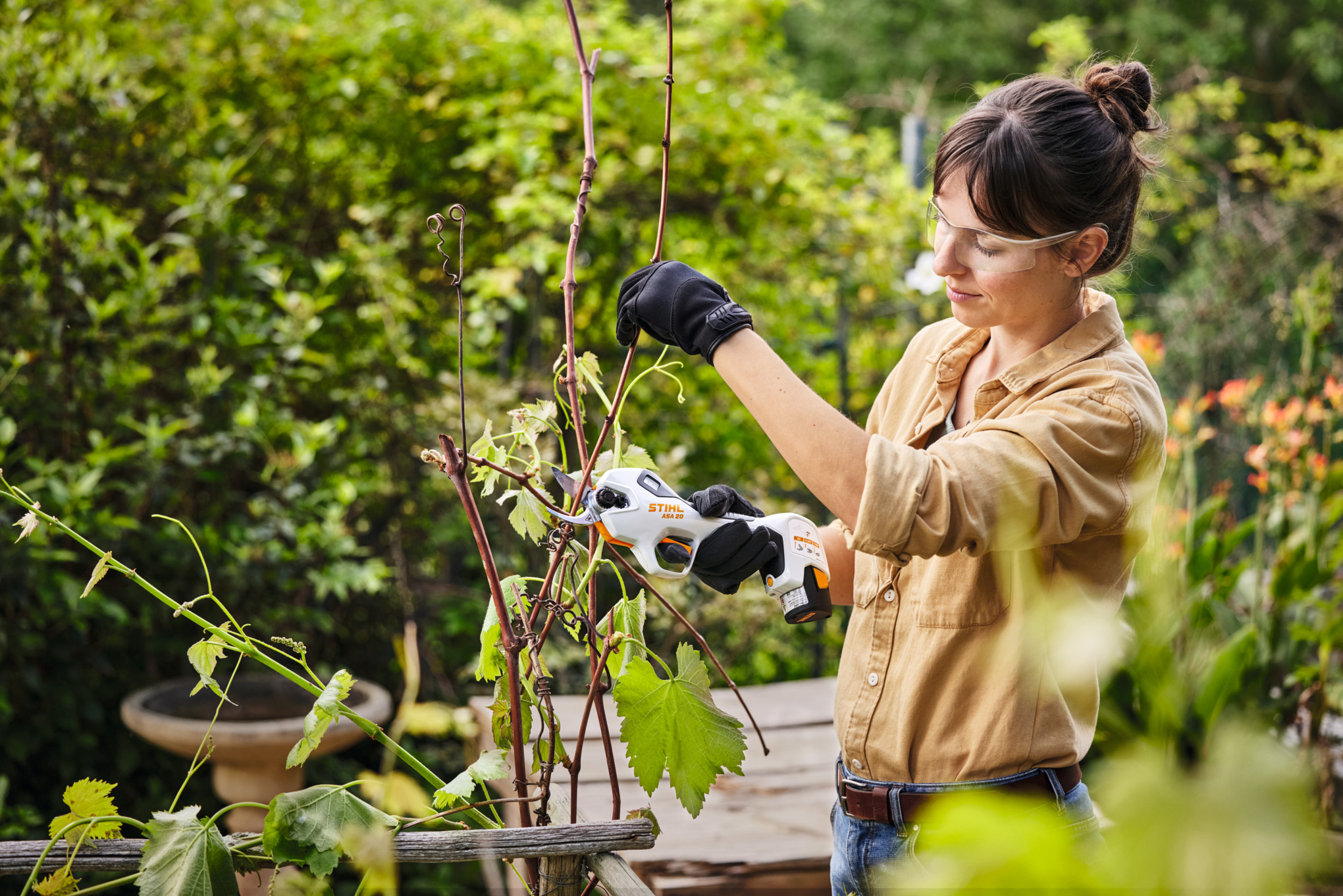 Frau benutzt STIHL ASA 20 Akku-Astschere im Garten