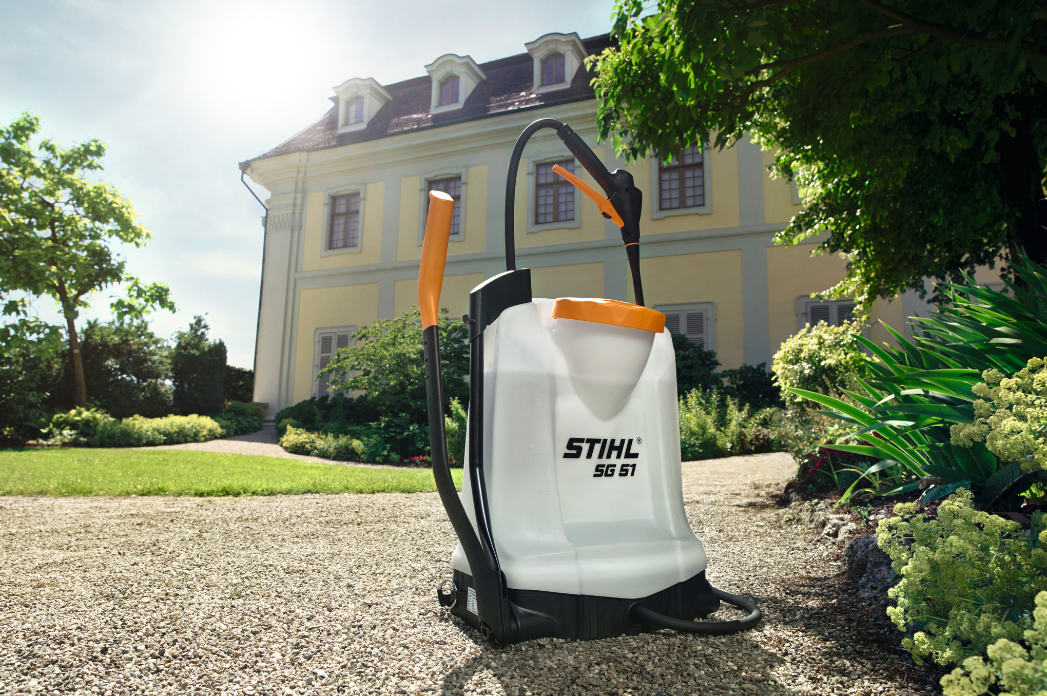 STIHL SG 51 Spritzgerät auf Kiesweg vor gelbem Herrenhaus im sonnigen Garten
