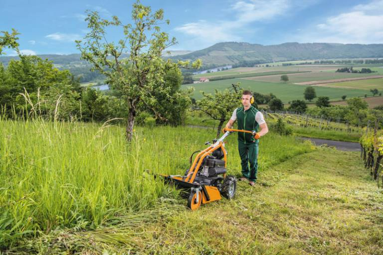 Mann bedient AS 63 2T ES Rasenmäher auf hügeliger Wiese mit Blick auf Tal