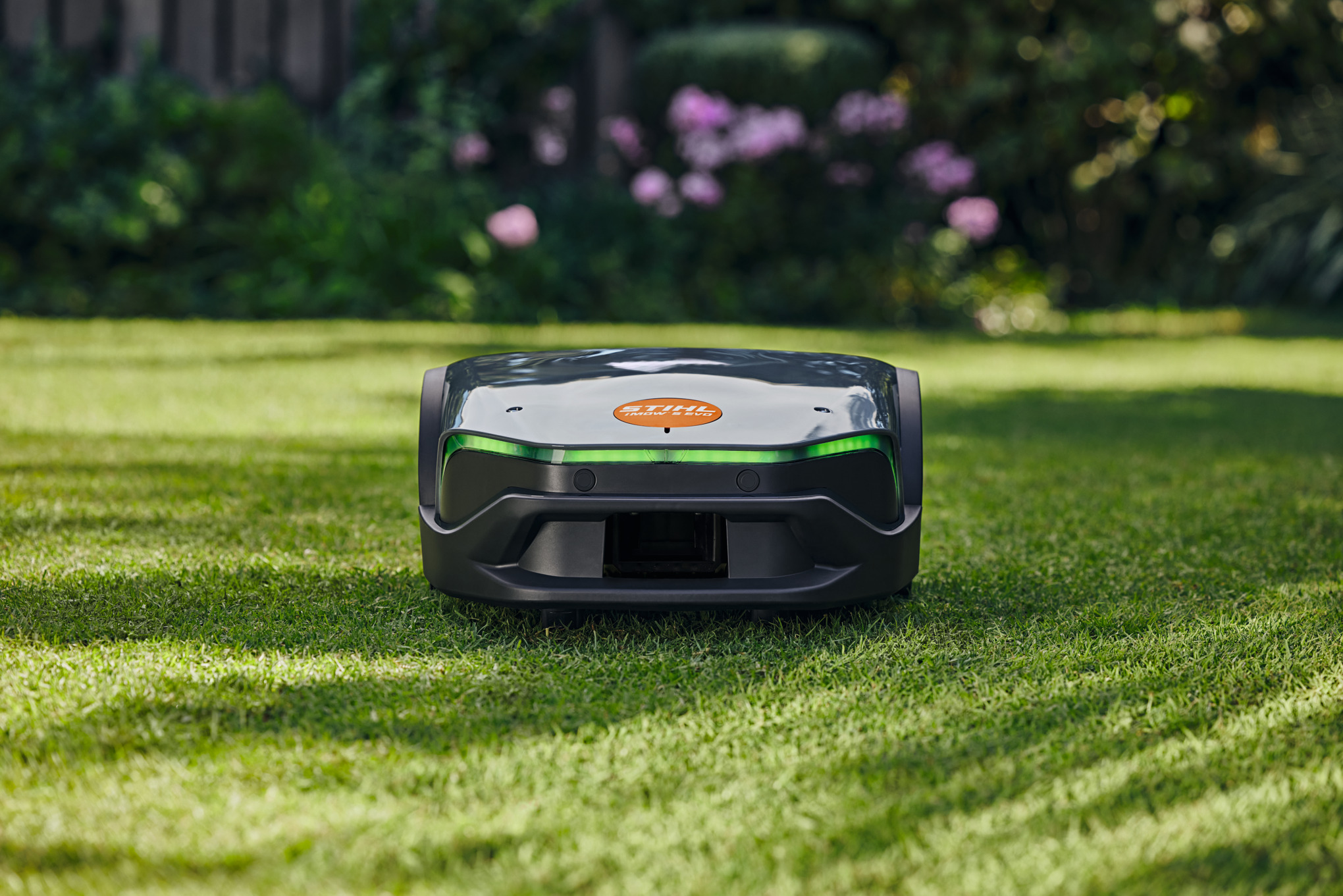 STIHL iMOW 6 EVO Mähroboter auf grünem Rasen mit Garten im Hintergrund