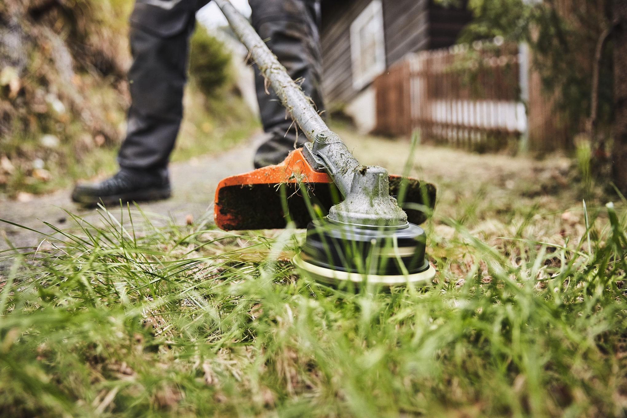 Stihl FS-KM AC C 26-2 Sense in Aktion beim Trimmen von Gras nahe einem Holzhaus