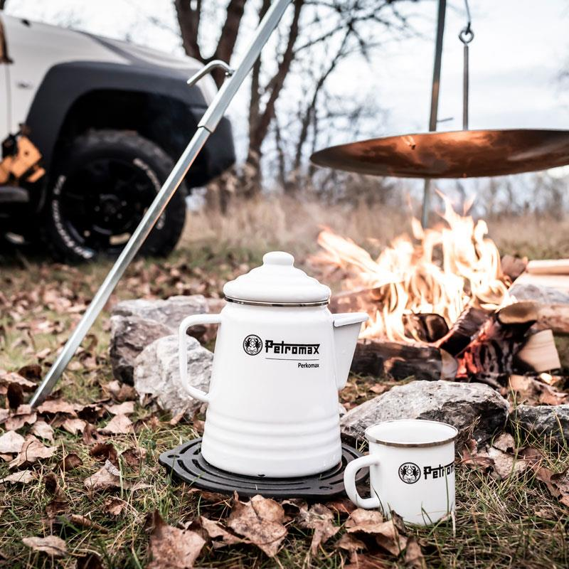Petromax Perkolator und Tasse neben Lagerfeuer im Freien