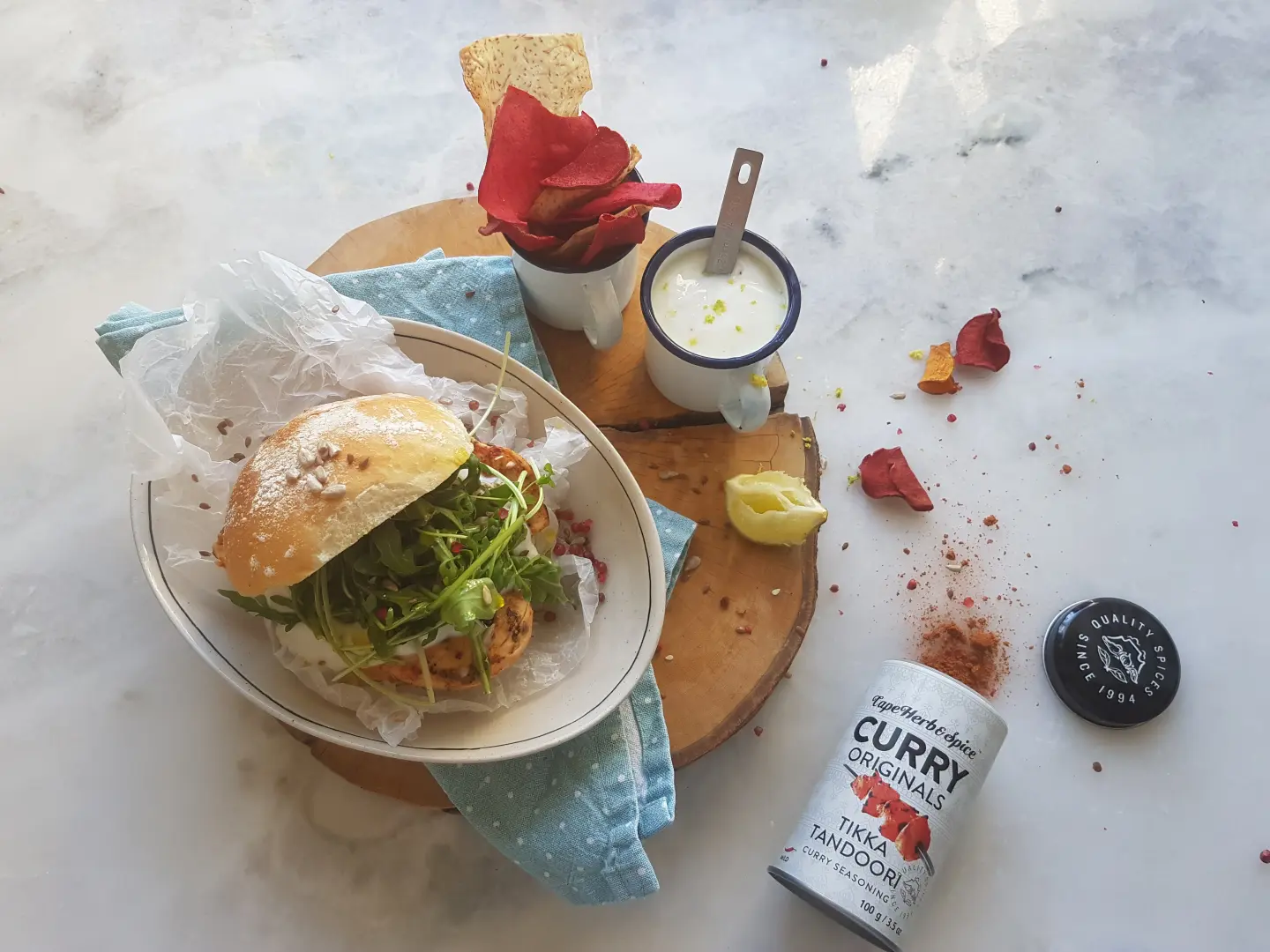 Sandwich mit Hähnchen und Rucola, rote Chips, weiße Sauce und Gewürzdose auf Marmortisch