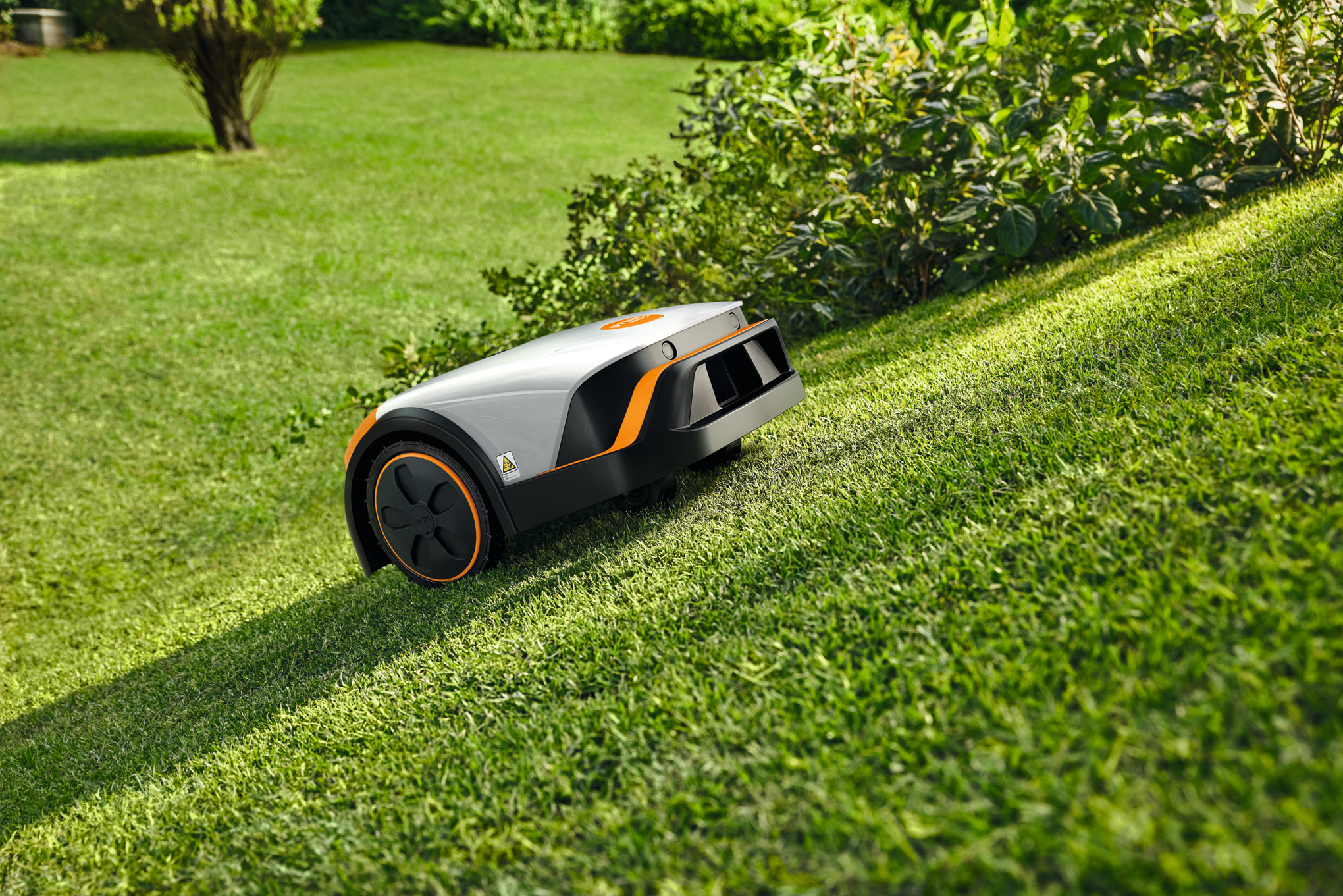 STIHL iMOW 4 Mähroboter mäht selbstständig einen grünen Rasen in einem sonnigen Garten