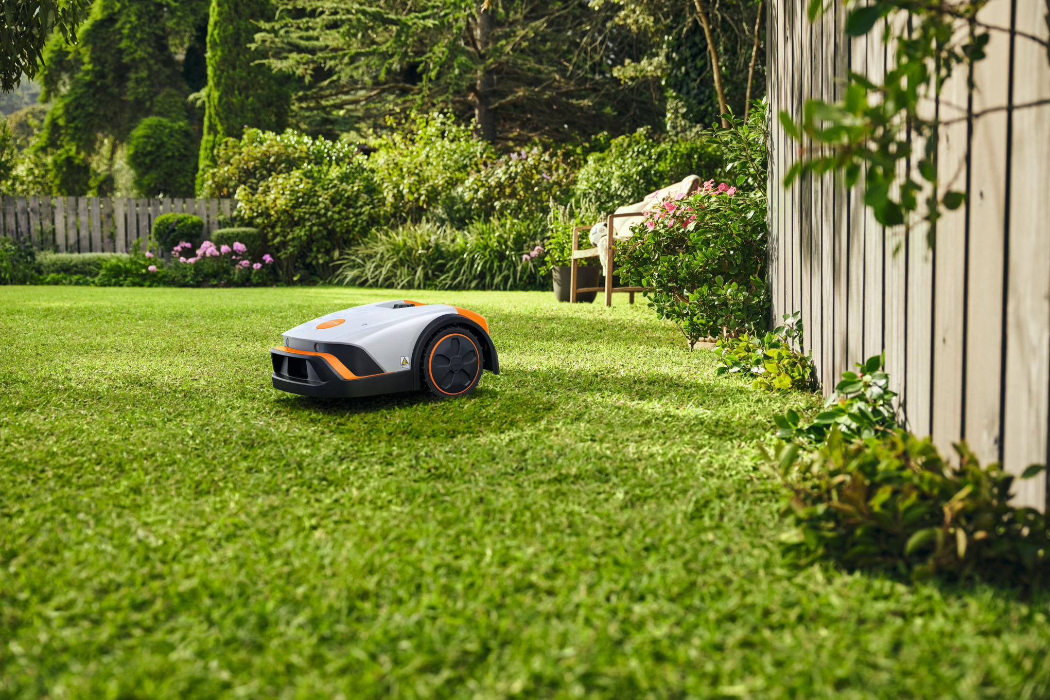 STIHL iMOW 4 Mähroboter mäht selbstständig einen grünen Rasen in einem schönen Garten