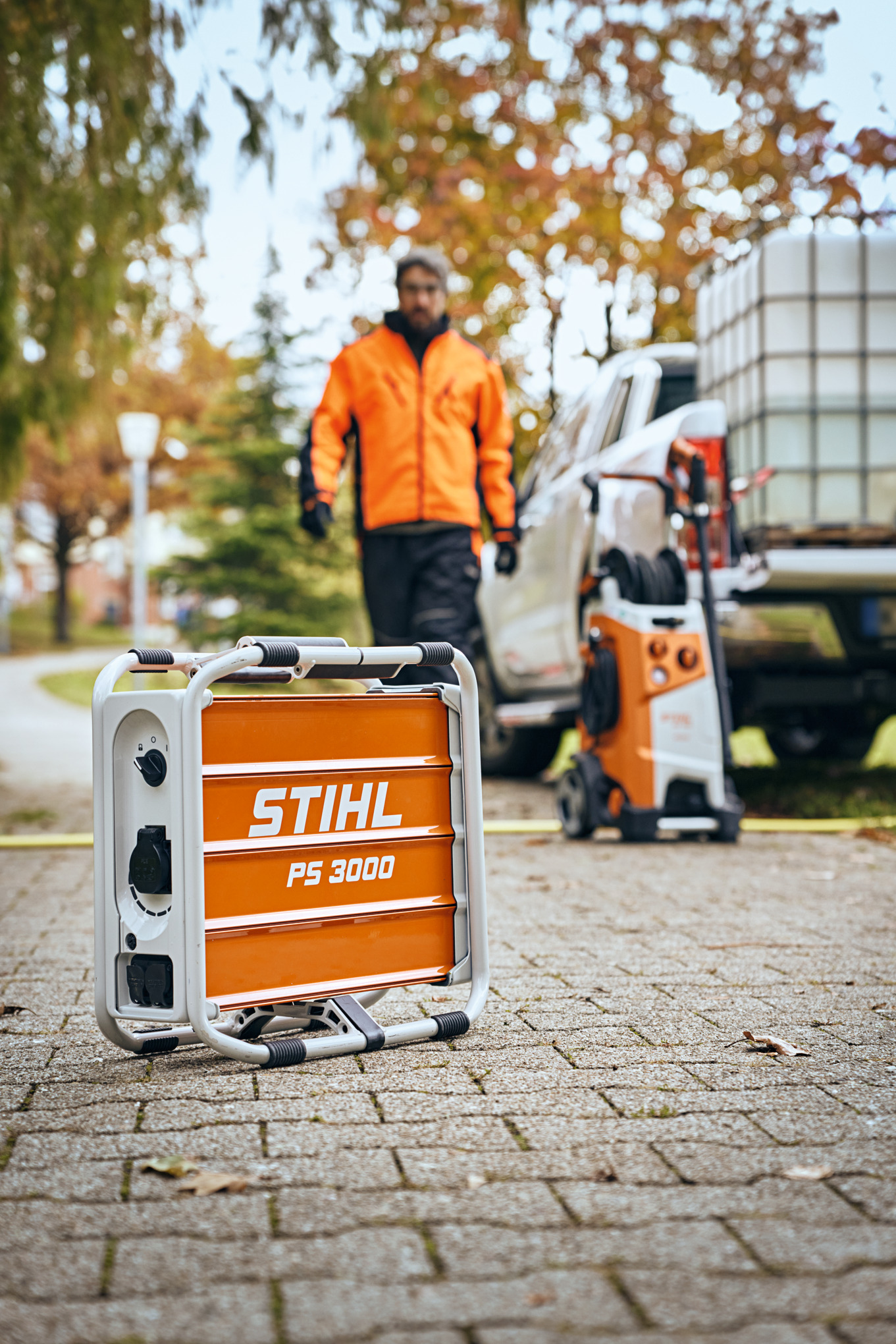 Mann in Arbeitskleidung steht hinter tragbarem Stromgenerator STIHL PS 3000 auf gepflastertem Weg